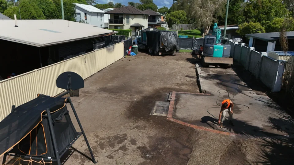 Worker landscaping backyard with paving and equipment.