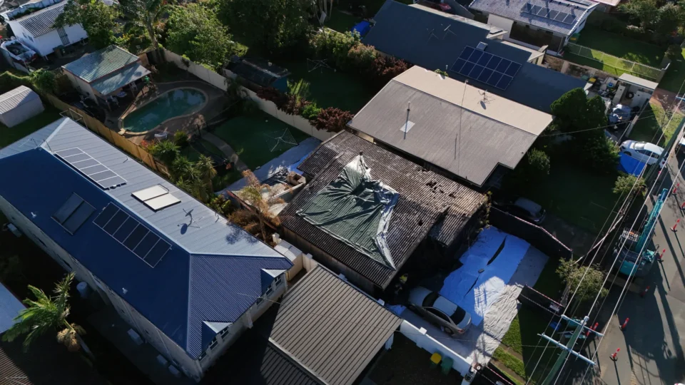 Damaged roof covered with tarp in residential neighborhood.